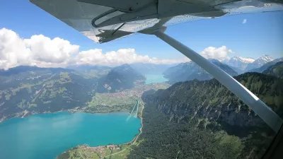 Blick aus einem Flugzeug auf einen türkisfarbenen See, umgeben von Bergen und Wäldern.